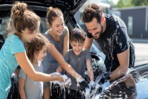 Famille souriante lavant une voiture après remboursement malus famille nombreuse.