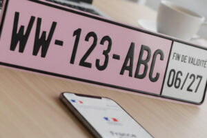 Modèle de plaque d’immatriculation provisoire WW rose avec date de validité affichée à droite sur un bureau.