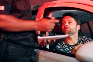 Un policier contrôle un automobiliste inquiet en voiture risquant une amende pour contrôle technique périmé.