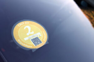 Gros plan d'une vignette Crit'Air 2 orange collée sur le pare-brise d'une voiture, montrant le QR code et la date.