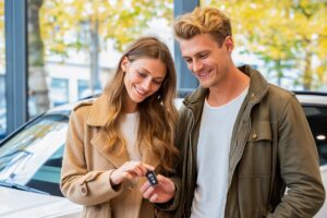 Un couple souriant échange les clés d'une voiture blanche, illustrant les démarches de carte grise entre époux.
