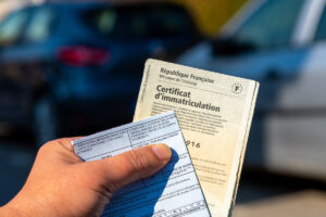Main tenant une carte grise française pour illustrer la modification des caractéristiques techniques de la carte grise