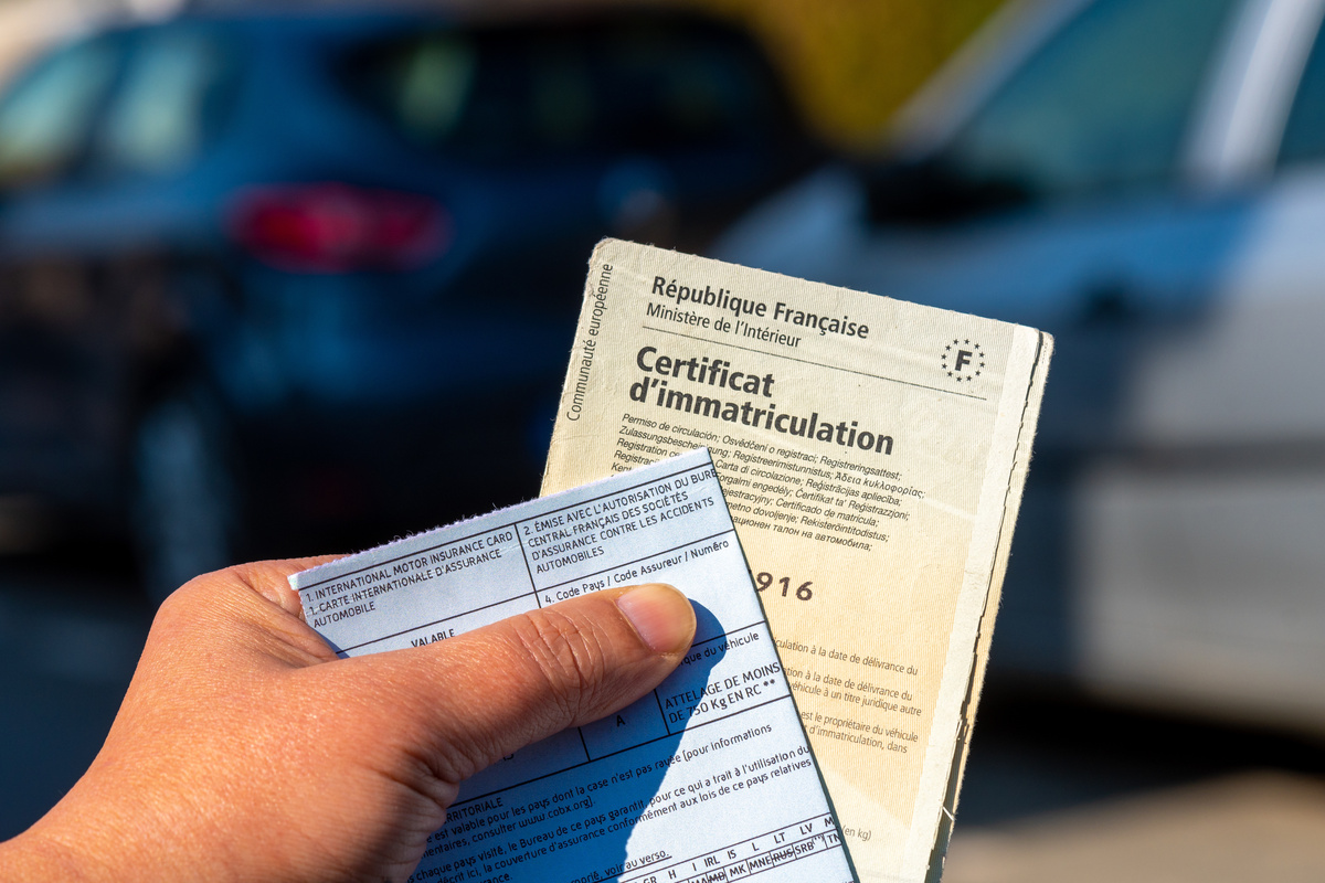 Main tenant une carte grise française pour illustrer la modification des caractéristiques techniques de la carte grise