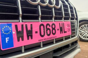 Gros plan sur une plaque WW rose d'immatriculation provisoire expirée fixée sur la calandre d'une voiture.